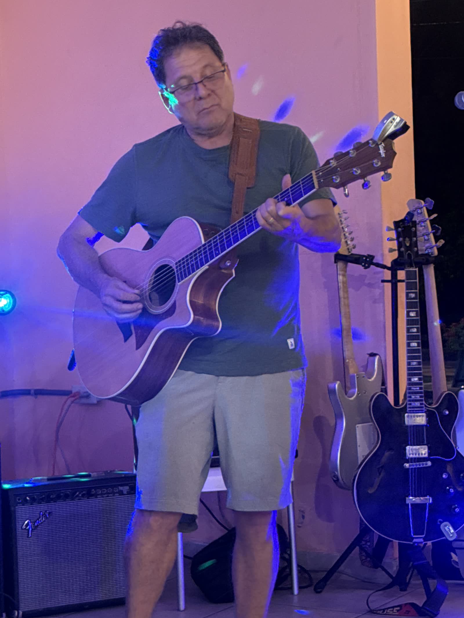 Foto real del músico tocando guitarra en vivo con luces moradas en La Divina Commedia Coronado